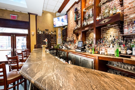 A bar with a long counter, wooden chairs, and a television mounted on the wall.