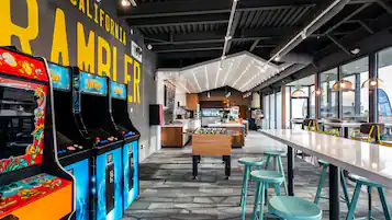 A retro-themed arcade with classic games, a foosball table, and a long communal table with stools.