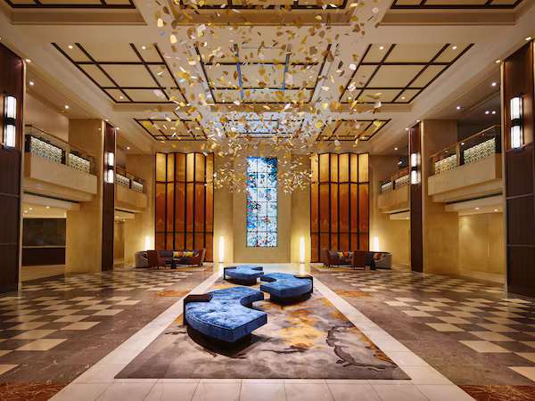 A spacious lobby with a checkered floor, a central seating area, and a large stained glass window.