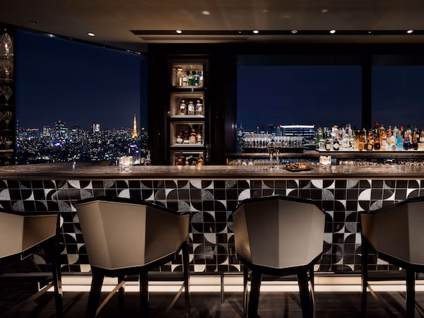 A bar with a city view, modern chairs, and a shelf with bottles.