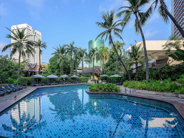 A swimming pool with lounge chairs and palm trees, surrounded by buildings.