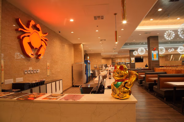 A restaurant interior with a crab decoration, a golden cat statue, and a counter with menus.