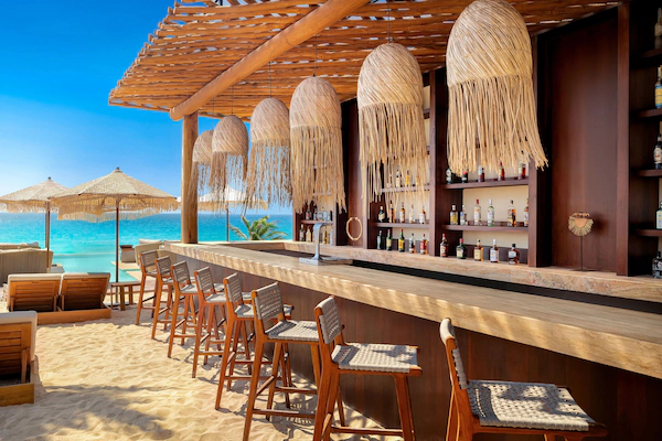 A beachside bar with wooden chairs and a bar counter, overlooking the ocean.