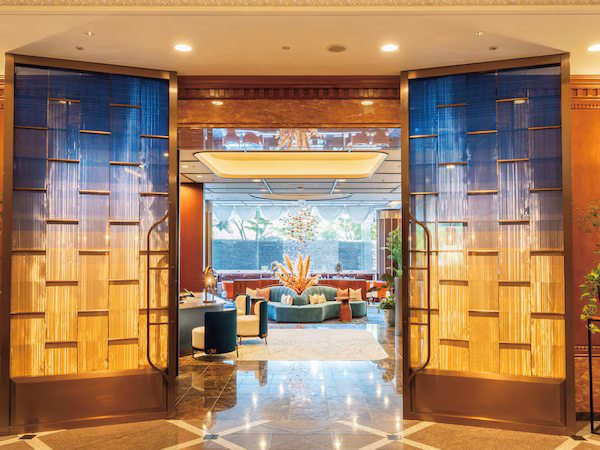 A hotel lobby with a grand entrance, a seating area with sofas and a coffee table, and a large window providing a view of the outdoors.