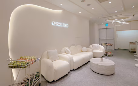 A modern hotel lobby with a white sofa, a round ottoman, and a cart with snacks.