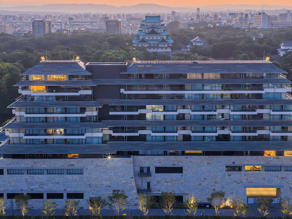 A multi-story building with a modern architectural design, featuring a mix of glass and stone facades, and a traditional pagoda structure in the background.