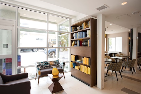 A modern interior with a seating area, a bookshelf, and a view through large windows.