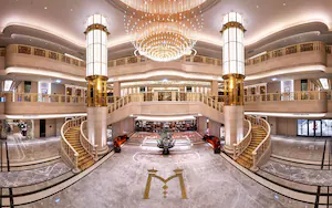 A multi-level hotel lobby with marble floors, a grand chandelier, and a central decorative piece.