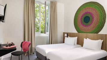A hotel room with two beds, a desk, a chair, and a large circular artwork on the wall.