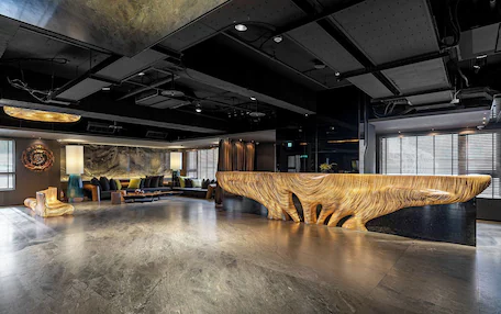A modern reception area with a unique wooden reception desk, seating area with sofas, and a large window providing natural light.