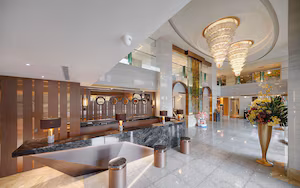 A modern hotel lobby with a marble reception desk, a large chandelier, and a decorative vase with flowers.