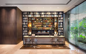 A modern library with a large bookcase, a desk with two chairs, and a large window with blinds.