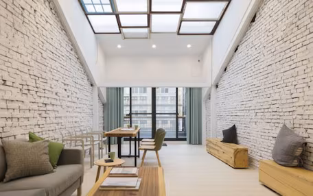 A modern living room with a high ceiling, exposed brick walls, and a large window providing a view of the city.