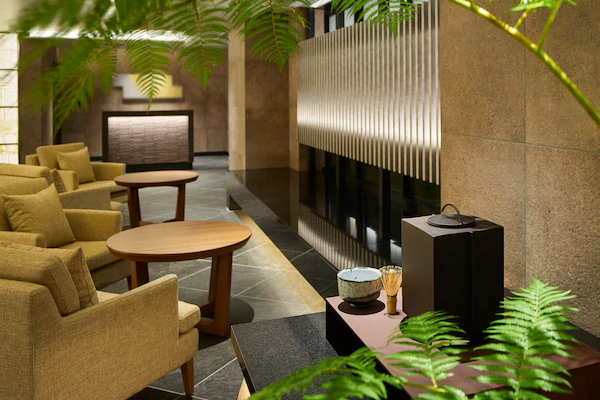 A modern lobby with sofas, a round table, a fireplace, and decorative plants.