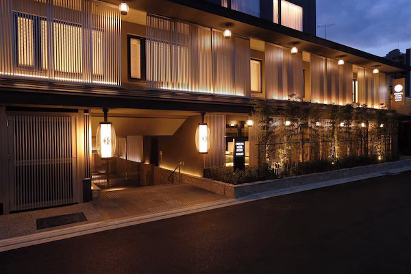A hotel entrance with a brick facade, outdoor seating area, and potted plants.