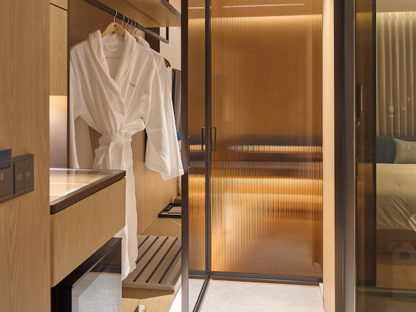 A modern hotel room with a wooden vanity, a robe hanging on the wall, and a sliding glass door leading to a balcony.