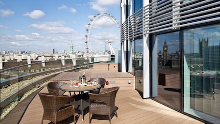 A rooftop terrace with a table set for dining, wicker chairs, and a view of the London Eye and Big Ben.