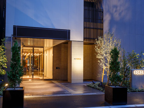 A modern hotel entrance with a glass door, a sign reading "FORZA", and a well-lit pathway leading to the entrance.