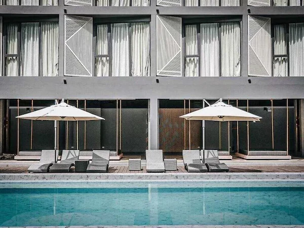 A modern building with a swimming pool, lounge chairs, and umbrellas.