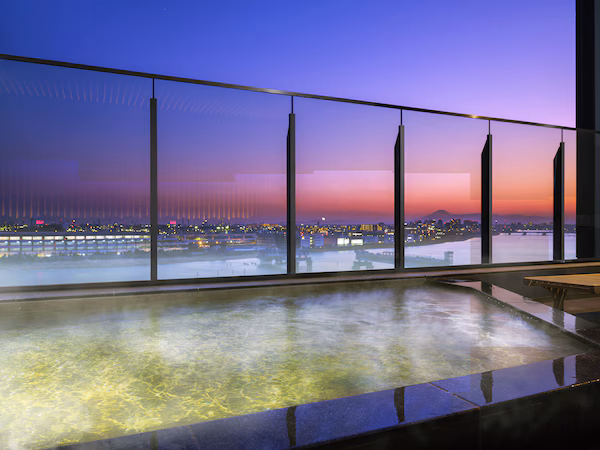 A panoramic view from a high-rise building with a glass railing overlooking a cityscape at dusk.
