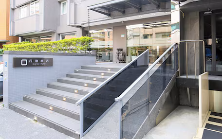 A hotel entrance with a tiled facade, a set of stairs with glass railings, and a sign indicating the hotel name.