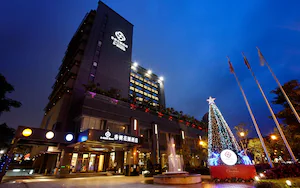 A hotel with a modern design, featuring a prominent logo on the facade, a large illuminated Christmas tree, and a fountain in the courtyard.