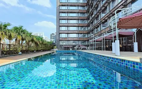 A modern hotel with a rooftop pool, palm trees, and a view of the city skyline.