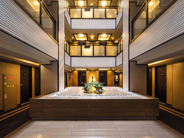 A modern hotel lobby with a central water feature, multiple elevators, and a glass-enclosed upper level.
