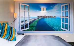 A bedroom with a large window revealing a beach scene with overwater bungalows.