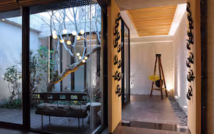 A modern interior with a glass door leading to a garden, a wooden bench, and a ladder against a textured wall.