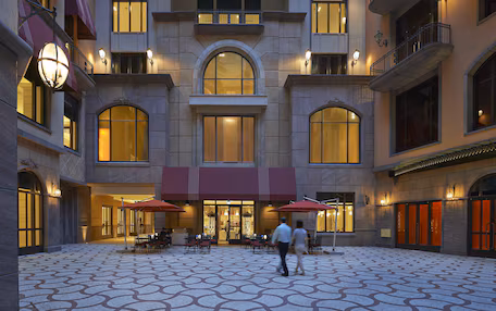 A hotel courtyard with a patterned floor, outdoor seating, and a central entrance with a red awning.